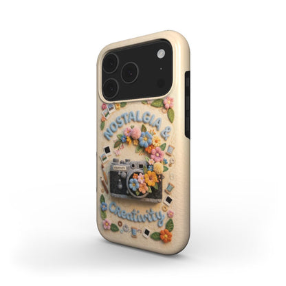 Dreidimensionale Ansicht einer iPhone-Schutzhülle in Creme-Weiß. Das Design zeigt ein aufwendiges Stickerei-Motiv mit einer Retro-Kamera, bunten Blumen und den Schriftzügen „Nostalgia & Creativity“. Die Hülle hat schwarze Ränder für die Tastenbedienung.